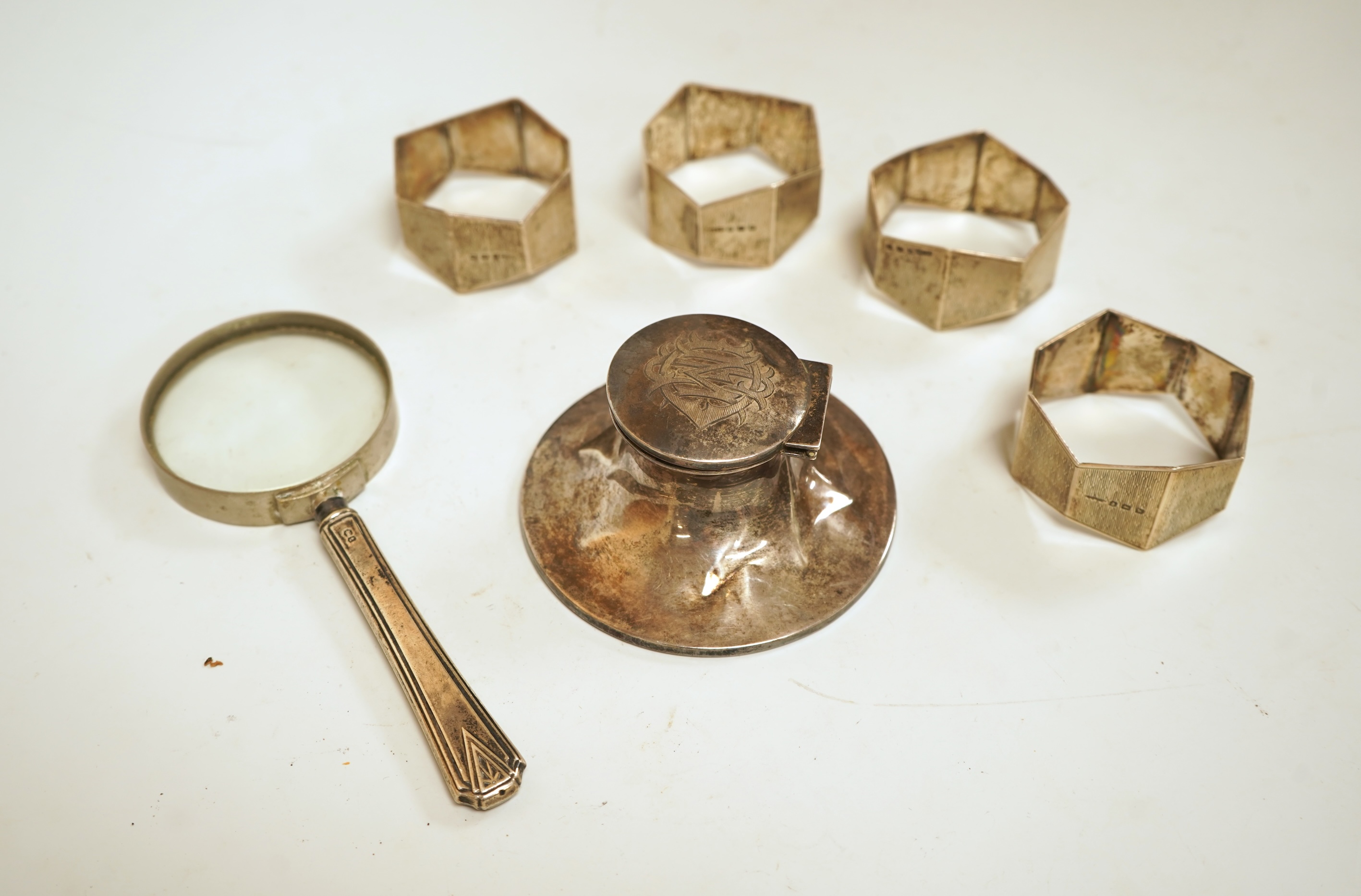 A small silver mounted capstan inkwell, a set of four George V engine turned silver napkin rings and a silver handled magnifying glass.
